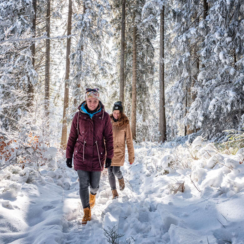 Zwei Freundinnen wandern durch den Winterwald bei Oberstaufen