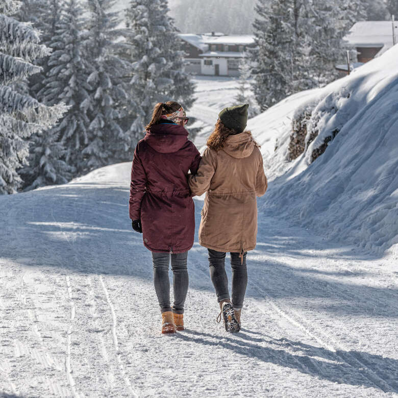 Zwei Frauen laufen auf einem geräumten Winterweg im Allgäu