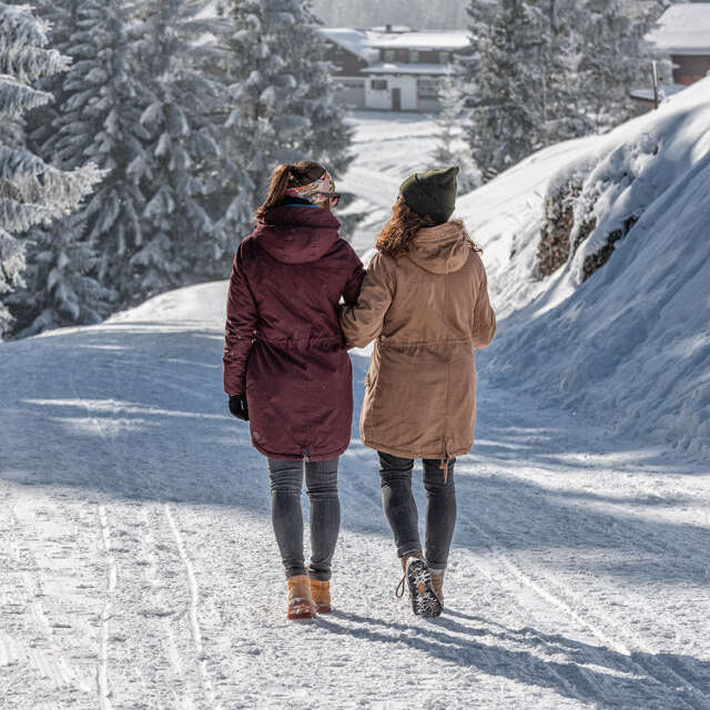 Zwei Frauen wandern auf einem geräumten Winterwanderweg in Oberstaufen