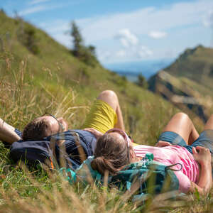 Paar liegt auf ihrer Hüttenwanderung in der Wiese im Allgäu und entspannt