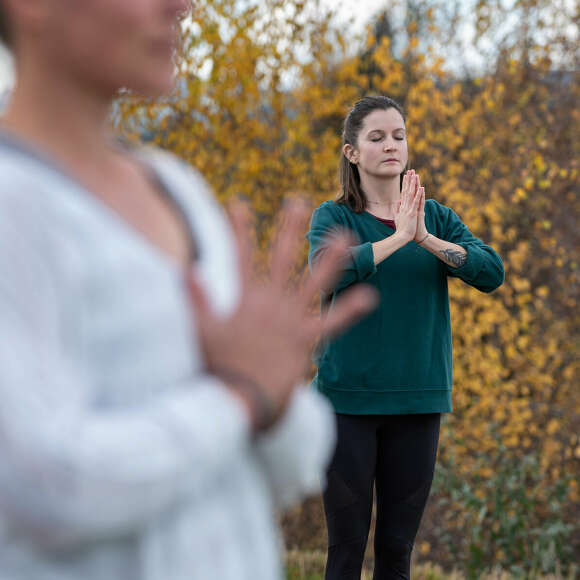 Frau macht Yoga auf einem Steg im Freien an einem Schwimmteich