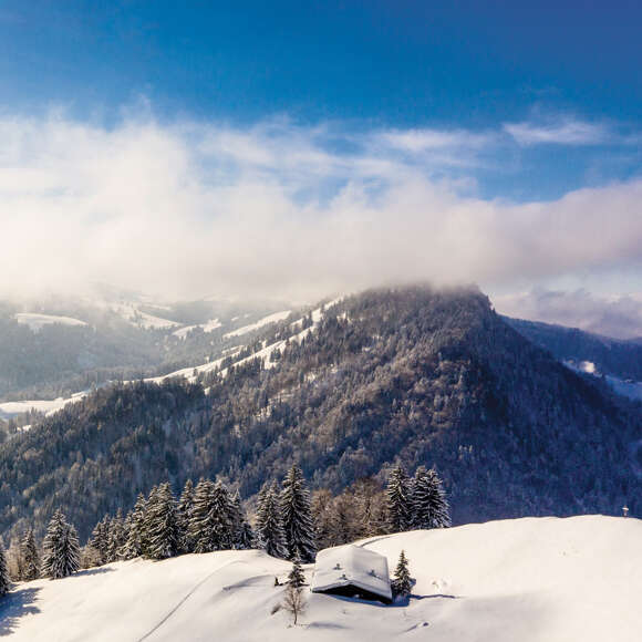 Winterlandschaft mit Sonne und Wolken in den Bergen von Oberstaufen.