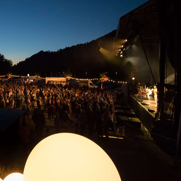 Open-Air Bühne mit Band bei Nacht mit Lichtershow. Davor Publikum.