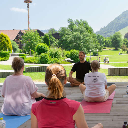 Gruppe meditiert im Freien mit Blick auf die Berge und den Kurpark von Oberstaufen im Allgäu