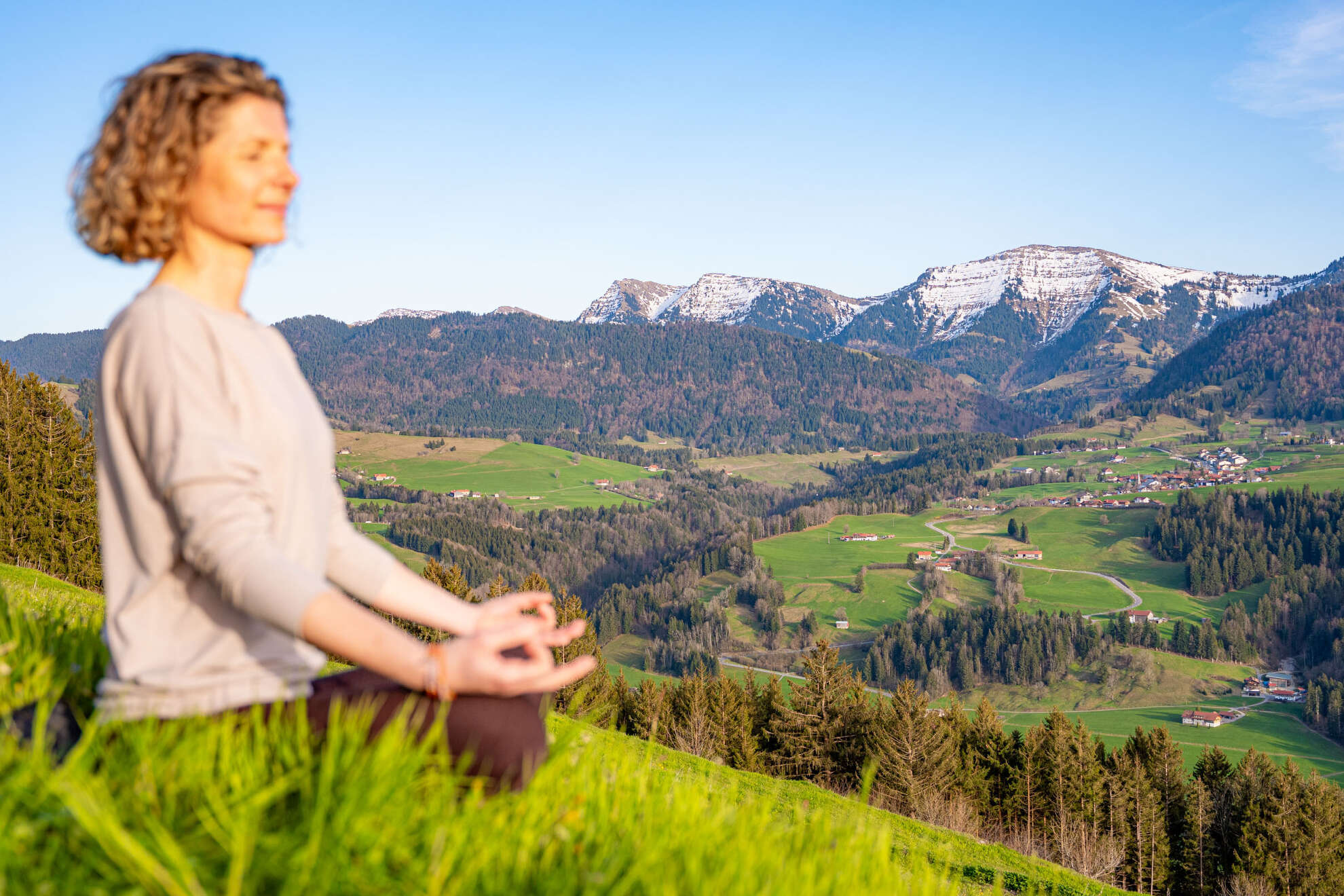 Achtsam in der Natur Frau im Loutus-Sitz am Paradies in Oberstaufen mit Weitblick auf die Berge