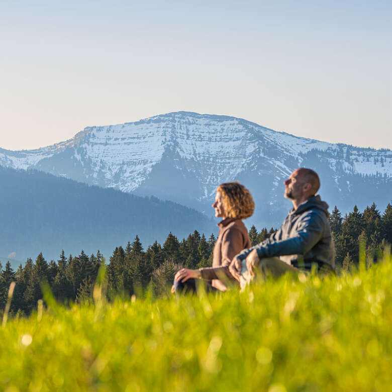 Der Natur ganz nah Mann und Frau sitzen im Lotus-Sitz in einer Wiese bei Oberstaufen mit Ausblick auf den Hochgrat