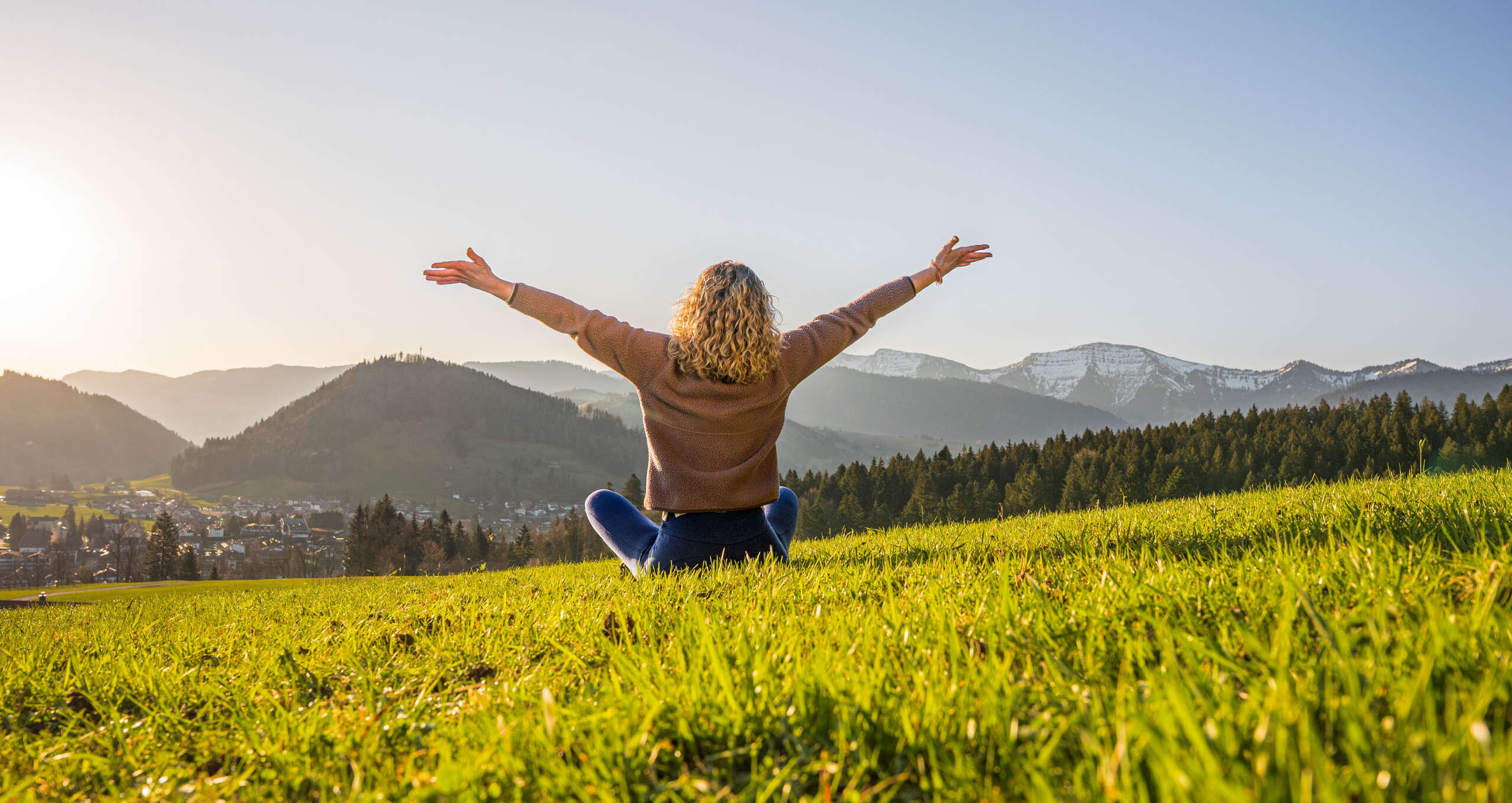 Frau entspannt in der Natur mit Weitblick auf Oberstaufen und die umliegenden Berge