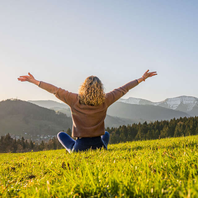 Frau entspannt in der Natur mit Weitblick auf Oberstaufen und die umliegenden Berge