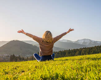 Frau entspannt in der Natur mit Weitblick auf Oberstaufen und die umliegenden Berge