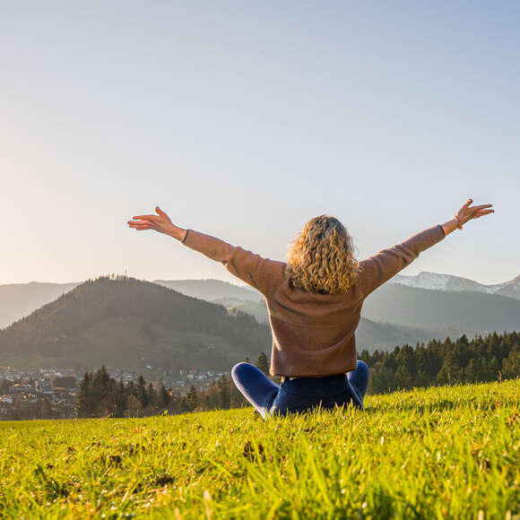 Frau entspannt in der Natur mit Weitblick auf Oberstaufen und die umliegenden Berge