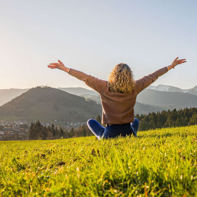 Frau entspannt in der Natur mit Weitblick auf Oberstaufen und die umliegenden Berge