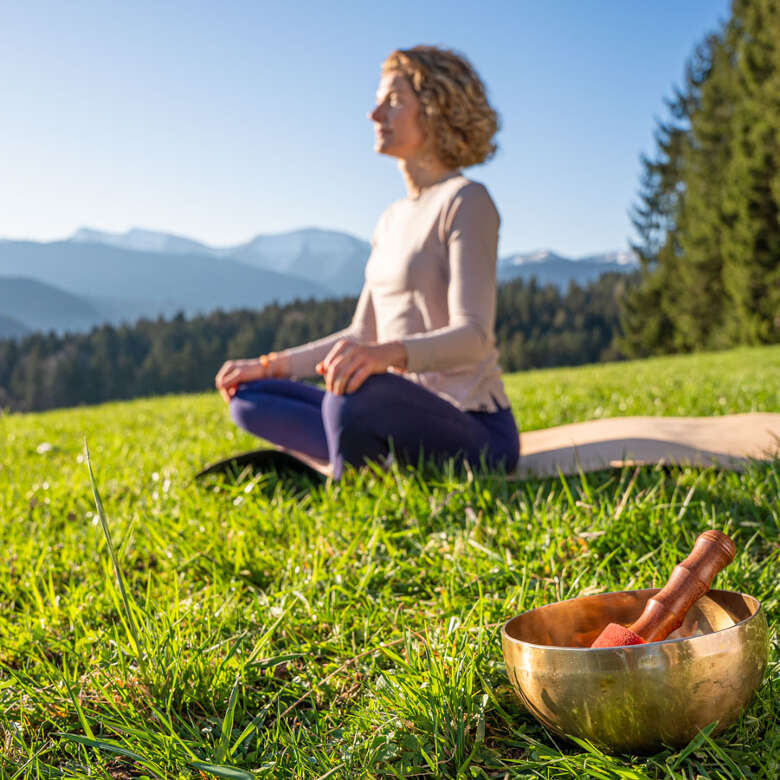 Zeit für Dich Frau im Lotus-Sotz auf einer Matte mit Klangschale in der Natur von Oberstaufen