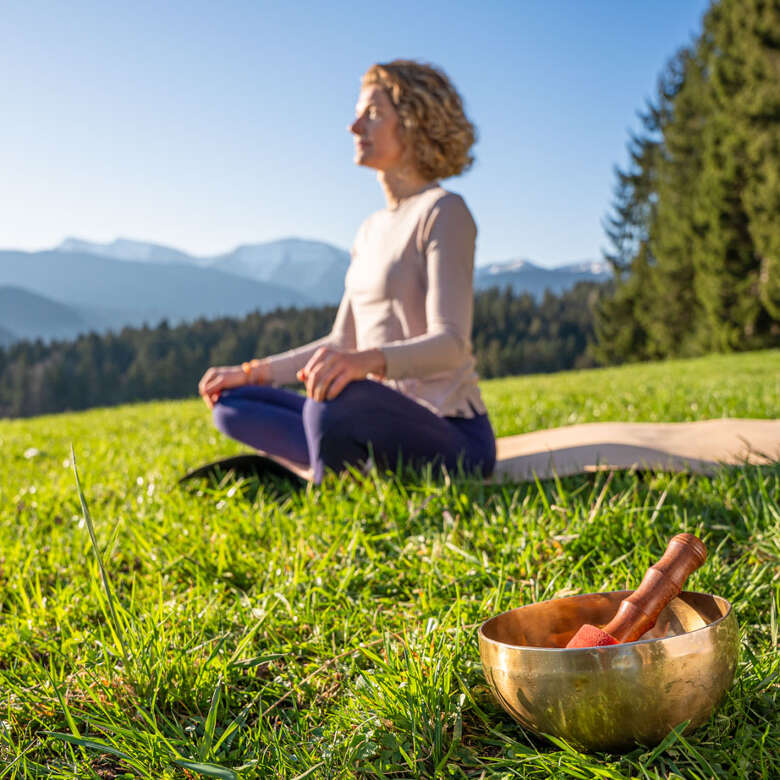 Zeit für Dich Frau im Lotus-Sotz auf einer Matte mit Klangschale in der Natur von Oberstaufen