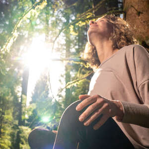 Frau lehnt an einem Baum im Wald in der Sonne