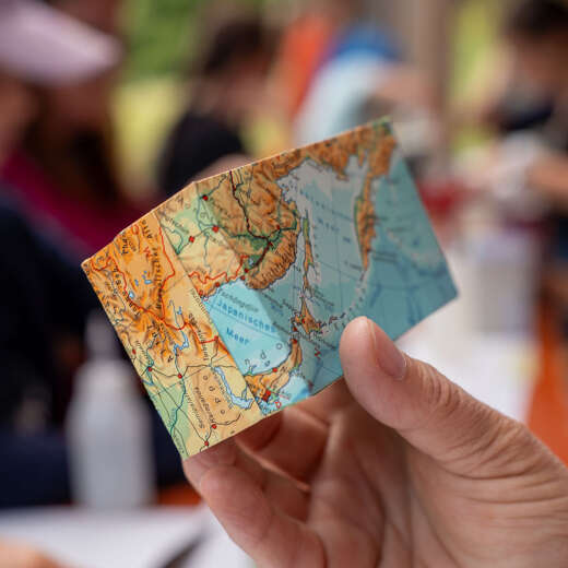 Hand hält ein gefaltetes Upcycling-Objekt aus einer alten Weltkarte beim Oberstaufener Weitblick