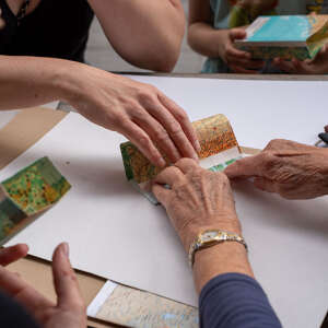 Mehrere Hände basteln gemeinsam beim Upcycling-Workshop mit alten Kalenderblättern beim Oberstaufener Weitblick