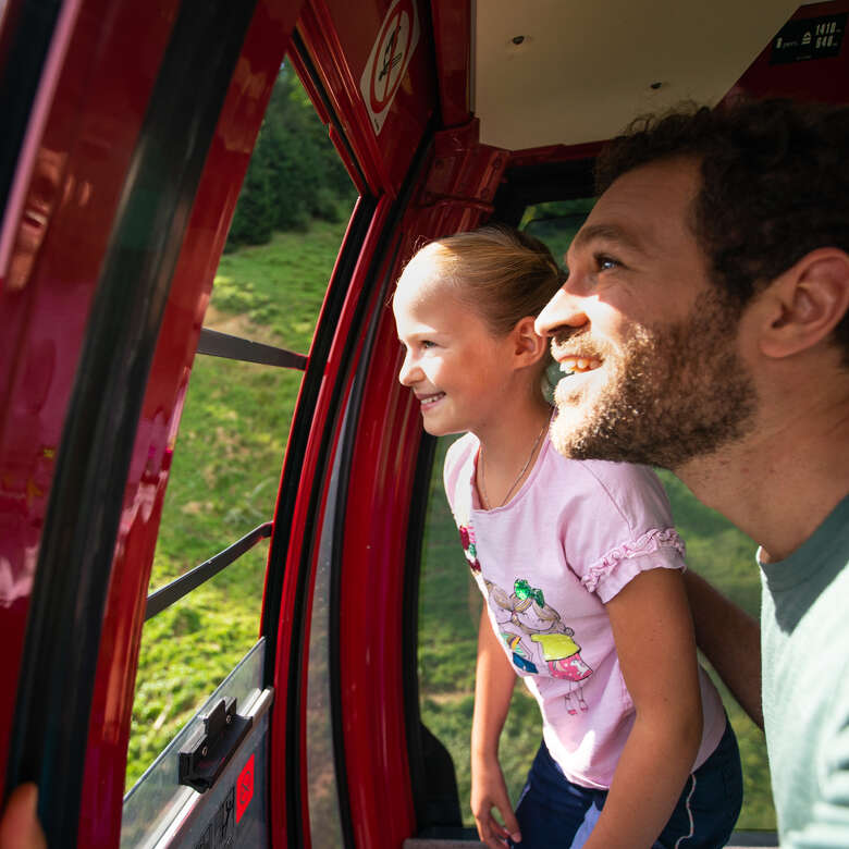Kind und Vater blicken aus dem Fenster der roten Gondel der Imbergbahn.