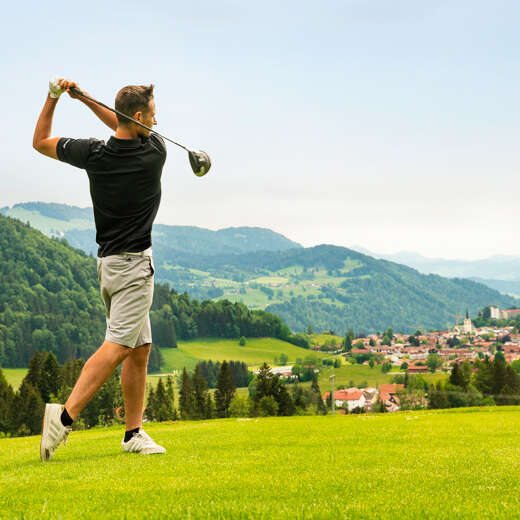 Golfer schlägt auf dem Golfpatz Oberstaufen mit Blick auf den Ort ab.