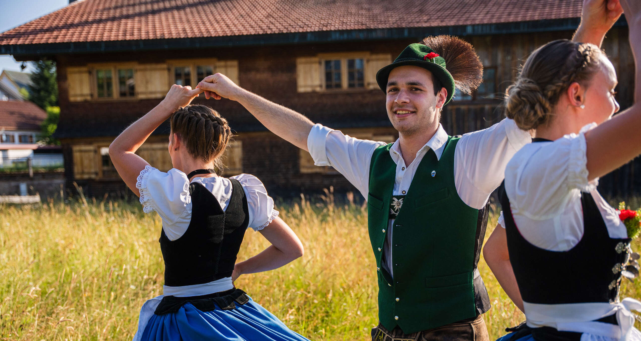 Trachtengruppe beim traditionellen Volkstanz in Oberstaufen – Männer in grüner Weste und Frauen im Dirndl tanzen auf einer Wiese