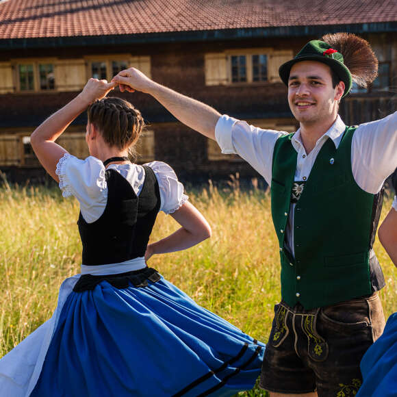 Trachtengruppe beim traditionellen Volkstanz in Oberstaufen – Männer in grüner Weste und Frauen im Dirndl tanzen auf einer Wiese