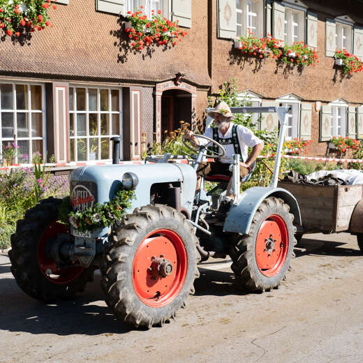 Ein Älpler auf einem Traktor fährt vor einem alten Bauernhaus.