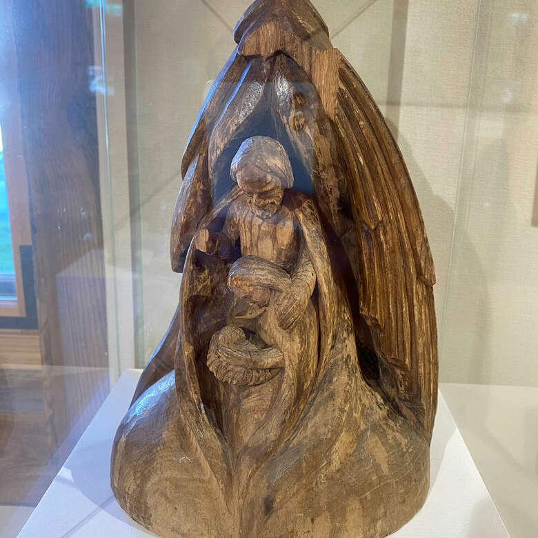 Eine aus Holz geschnitzte Krippe steht in einer Glasvitrine.