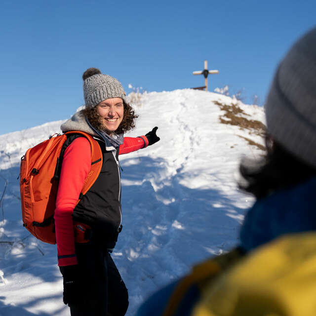 Frau zeigt ihrer Freundin das Gipfelkreuz im Winter in Oberstaufen
