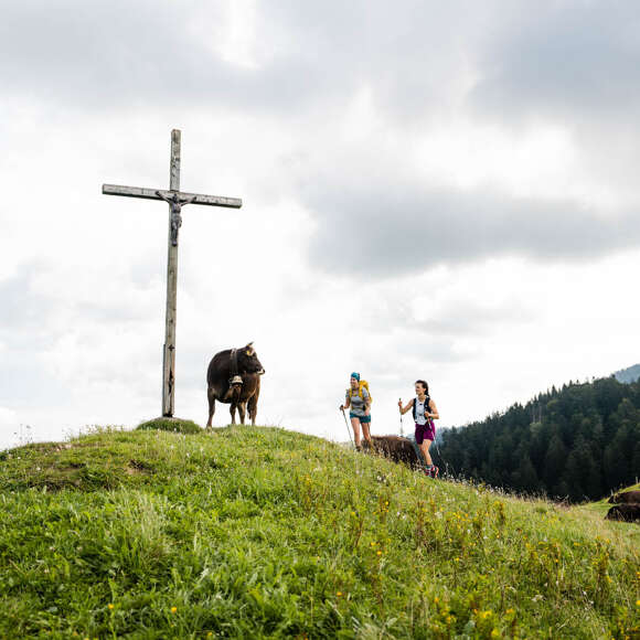 Zwei Frauen kommen an einem Gipfelkreuz an.