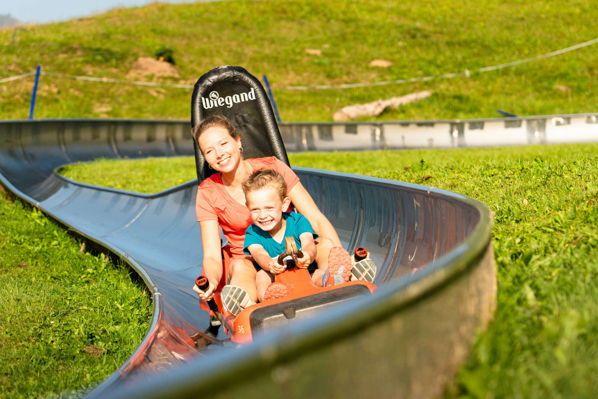 Frau fährt mit Kind die Sommerrodelbahn am Hündle im Sommer.