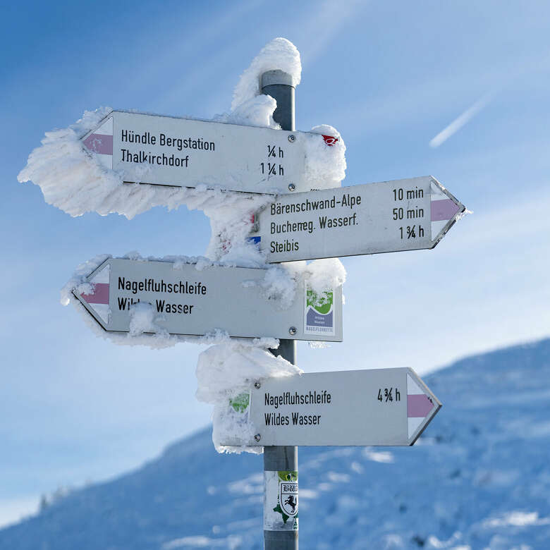Der verschneite Wegweiser weist die Winterwanderwege am Gipfelkreuz am Hündle aus.