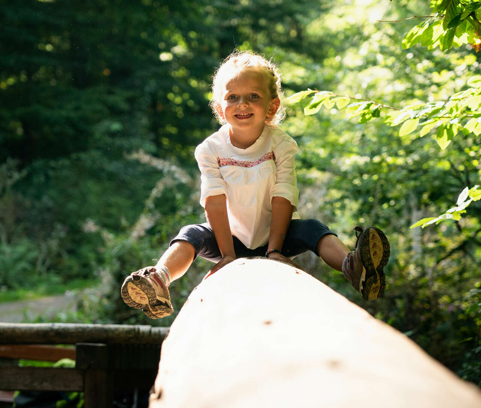 Kleines Mädchen spielt auf Baumstamm beim Wandern in Oberstaufen