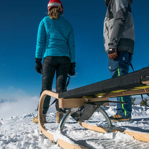 Zwei Personen mit Skioutfit und Rodeln stehen im Schnee mit Blick in die Ferne.