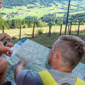 Ein Wanderer blickt in eine Wanderkarte von Oberstaufen. Er sitzt in der sommerlichen Natur.