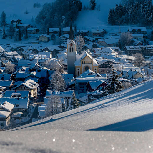 Der Ortskern und die Kirche von Oberstaufen verschneit im Winter.