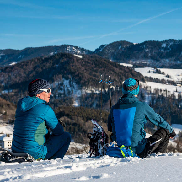 Schneeschuhwanderer sitzen im Schnee und schauen in die verschneite Landschaft.