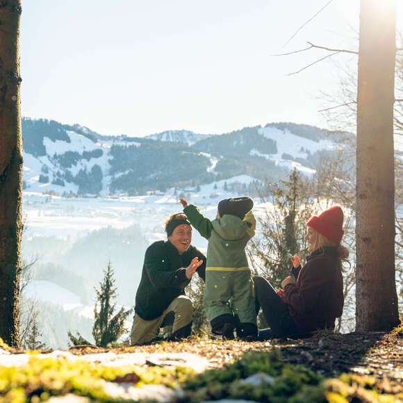 Familie macht Pause vom Wandern im Wald mit Blick auf die Berge von Oberstaufen