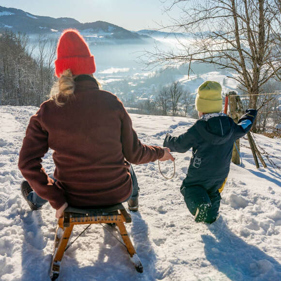 Rodeln mit Kind am verschneiten Staufen mit Ausblick auf Oberstaufen