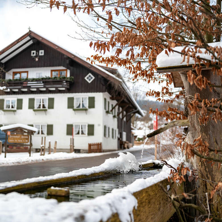 Verschneite Dorfmitte Thalkirchdorfs mit eisigem Brunnen im Allgäu.