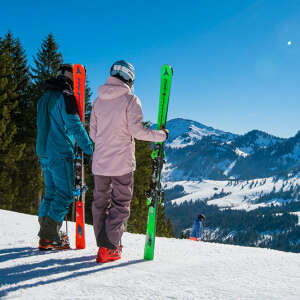Zwei Skifahrer an ihre Ski gelehnt schauen in die Ferne auf Bergpanorama im Schnee.