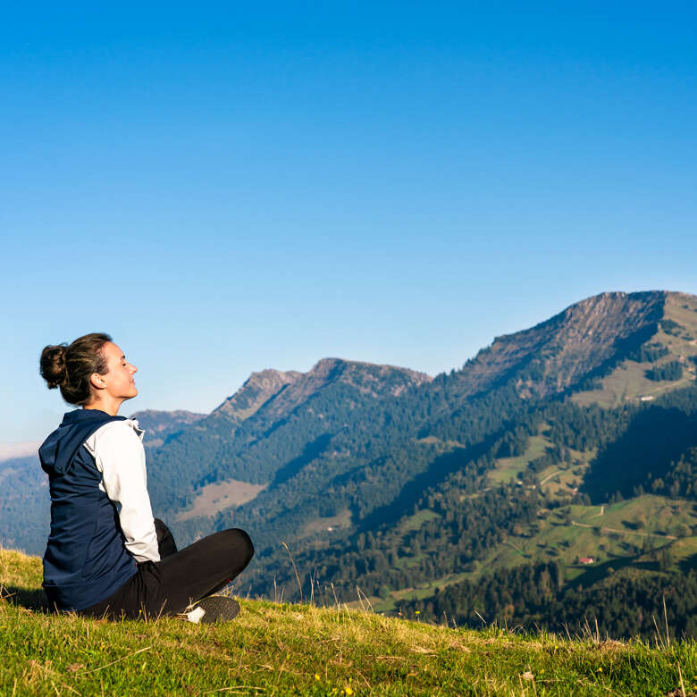 Vitalität in Oberstaufen Frau sitzt auf einer Wiese im Naturpark Nagelfluhkette und genießt die Aussicht.