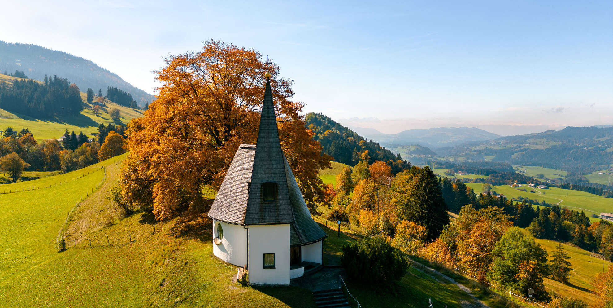 Kapelle in herbstlicher Landschaft bei Oberstaufen Kleine Kapelle mit spitzem Turm inmitten herbstlicher Hügel bei Oberstaufen im Allgäu, umgeben von buntem Laub und weiter Aussicht