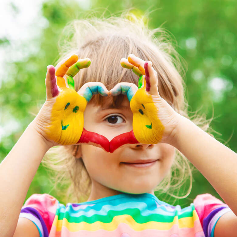 Kind formt ein Herz mit bunt bemalten Händen im sommer