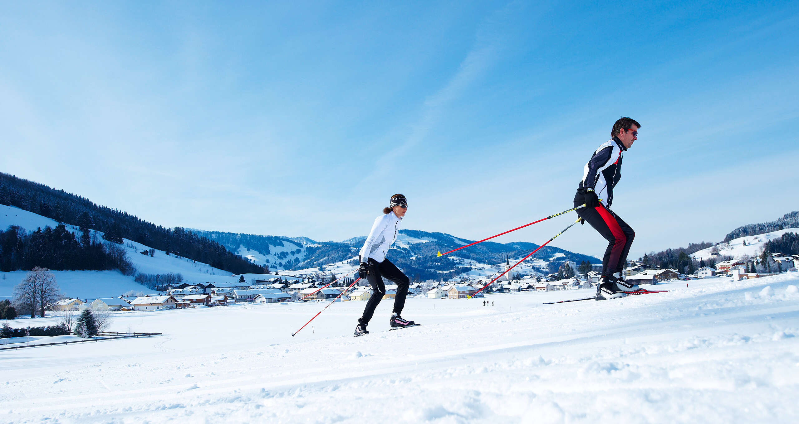 Zwei Langläufer auf der Loipe bei Oberstaufen an einem sonnigen Wintertag.