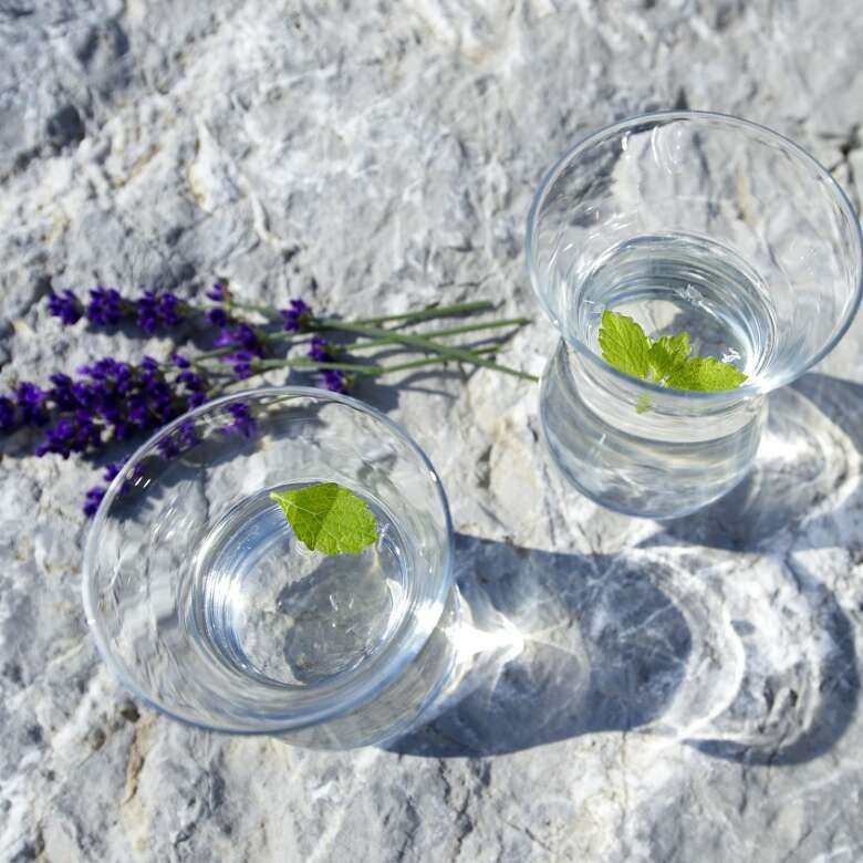 Wasser - alles andere als langweilig Blick von oben auf zwei volle Wassergläser mit einem Minzblatt, daneben Lavendel.