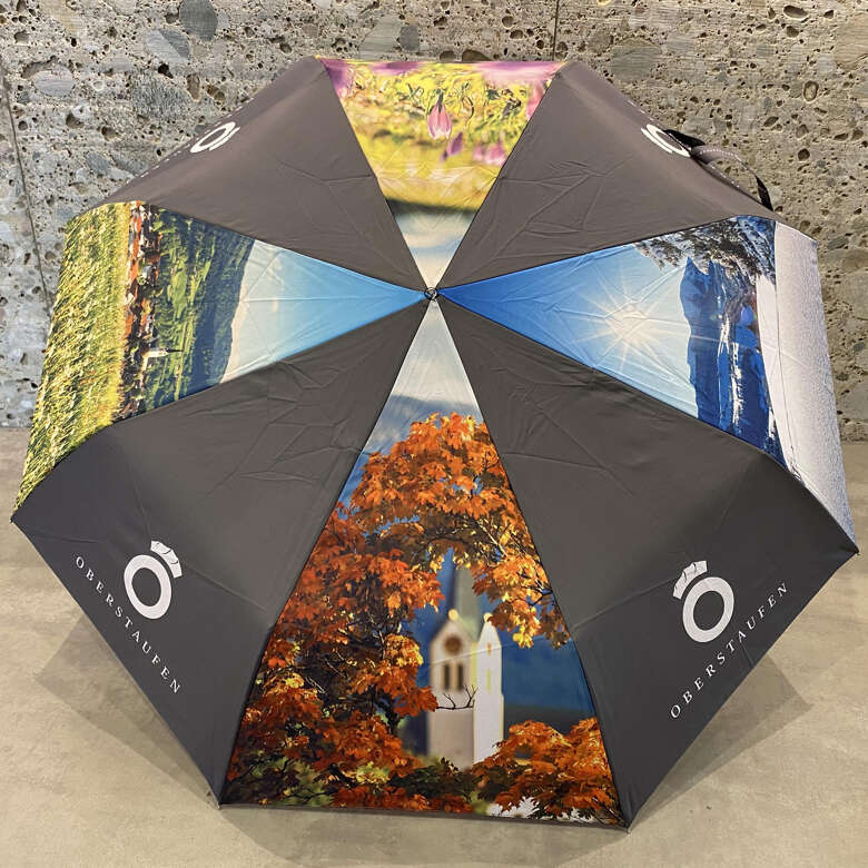 Aufgespannter Schirm mit grauen Flächen und Oberstaufen Logo, abwechselnd mit Bildern.