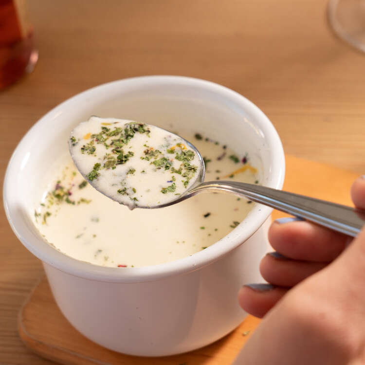 Aus einer Käsesuppe in Terrine mit Kräutern wird gerade ein Löffel voll genommen.