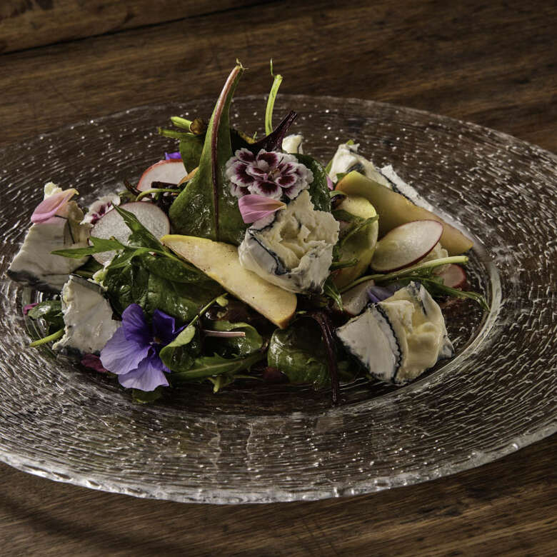 Allgäuer Wildkräutersalat mit Ziegenkäse auf einem Glasteller angerichtet