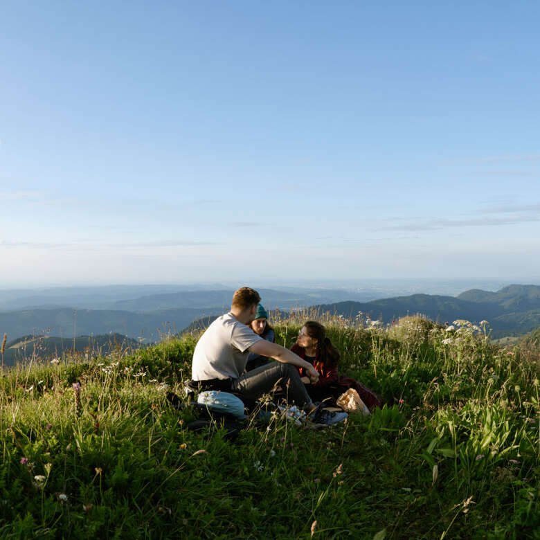 Drei Personen sitzen auf dem Hochgrat bei Sonnenuntergang.