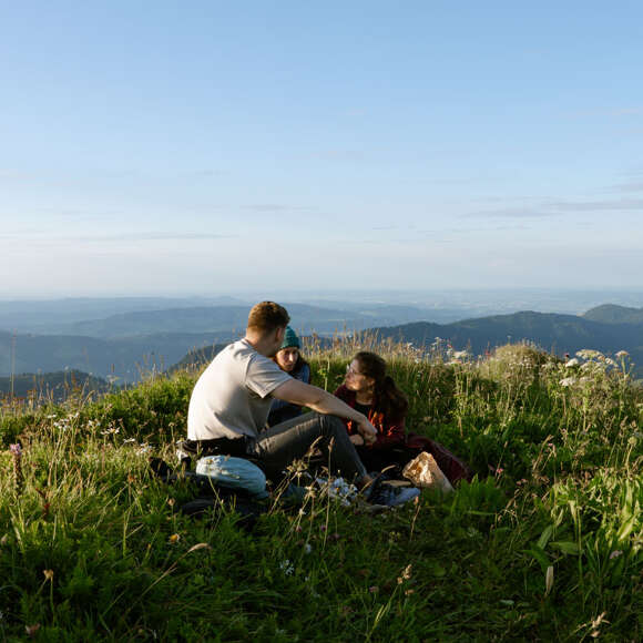 Drei Personen sitzen auf dem Hochgrat bei Sonnenuntergang.