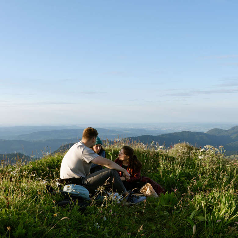 Drei Personen sitzen auf dem Hochgrat bei Sonnenuntergang.